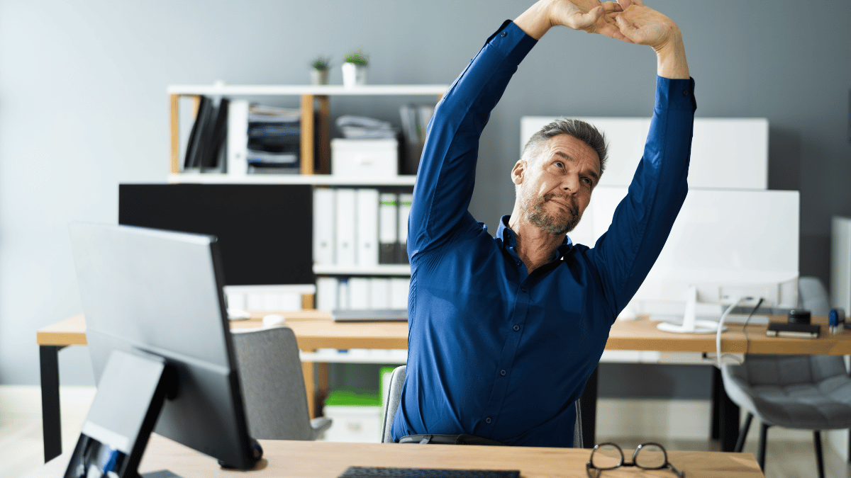 Individuals stretching arms beside standing-height desks indoors